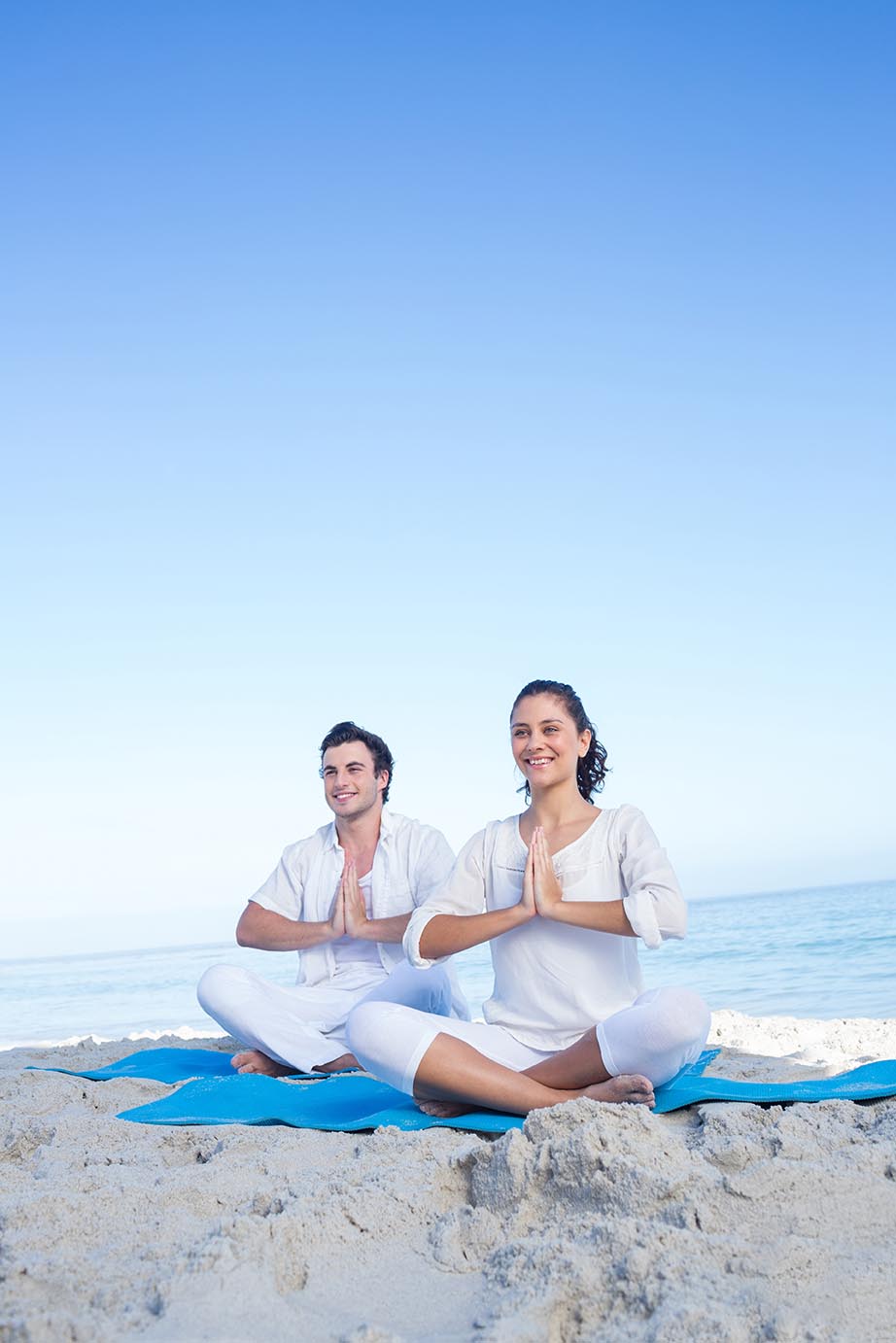 Happy couple doing yoga beside the water at the beach